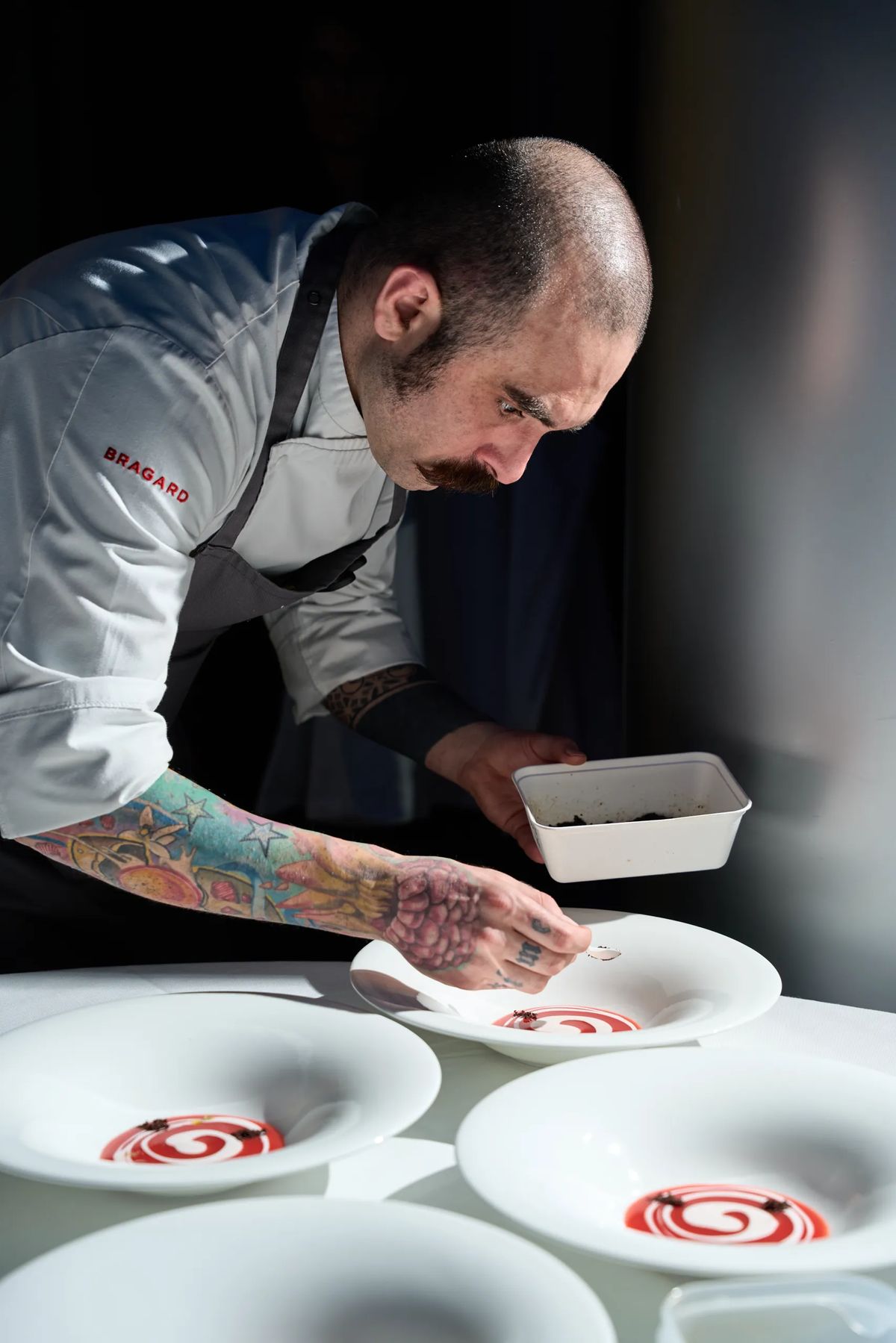 Chef con tatuaggi che impiatta con spirale di salsa rossa