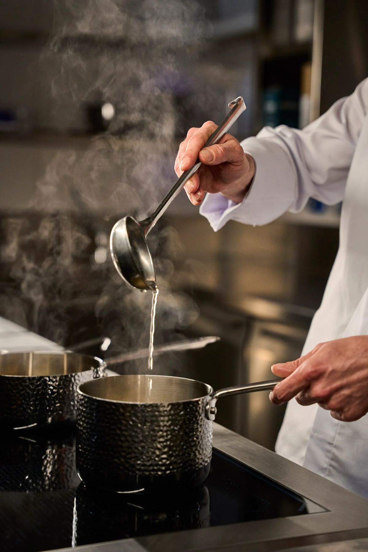 Chef che versa brodo fumante con mestolo su pentola in acciaio