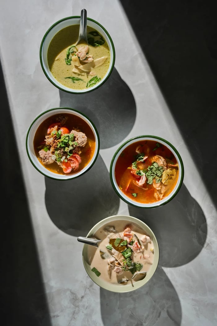 Quattro zuppe thai: curry verde, tom yam, curry rosso e tom kha con ombre geometriche — fotografia menu Thai Lounge Milano Lombardia